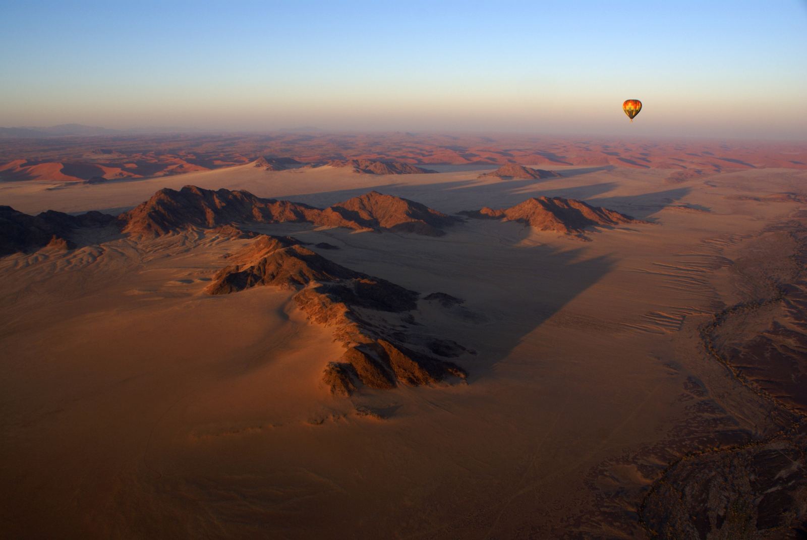 A hot air balloon above the dune ridges of the Namib, mountains hazy behind